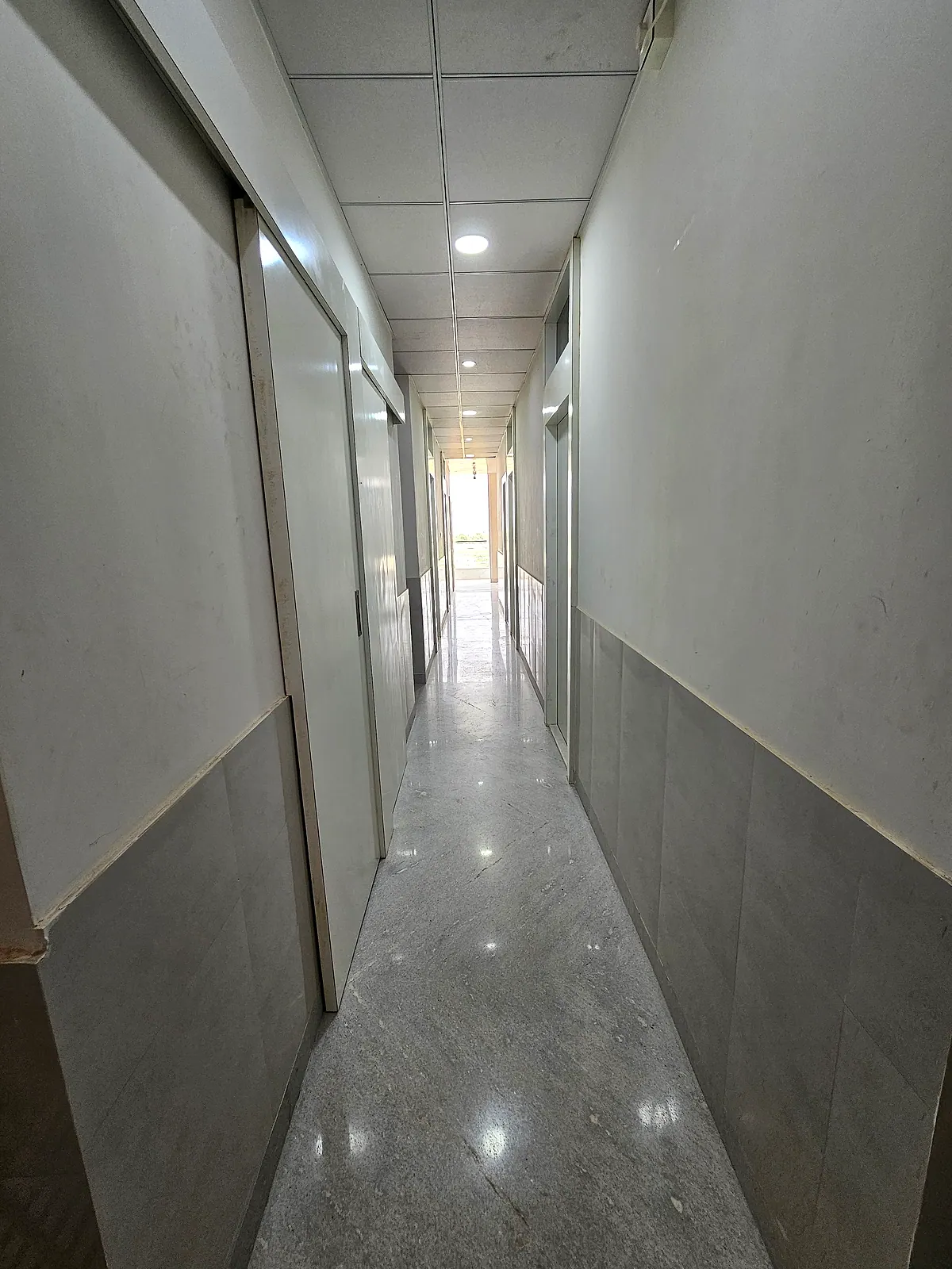 Long finished interior corridor with room doorways and ceiling lights