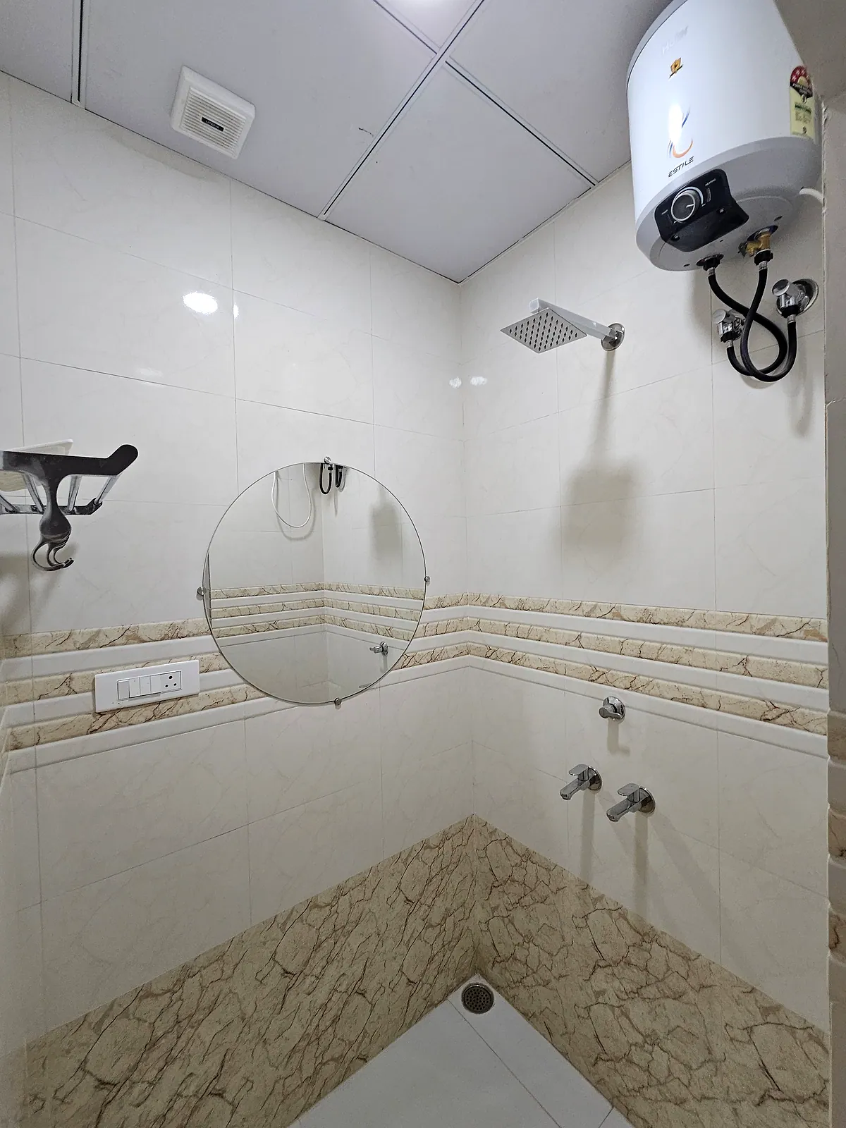 Separate tiled shower area with overhead shower, wall taps, mirror and geyser fittings